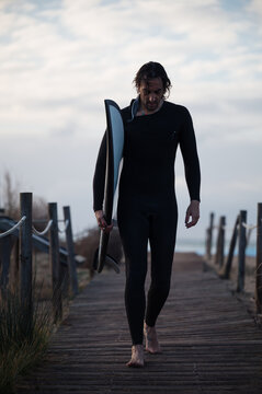 Surfer walking on wooden footbridge carrying surfboard at sunset