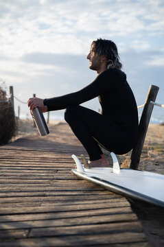 Surfer resting on wooden walkway with surfboard