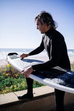 Surfer waxing his surfboard on the beach before surfing