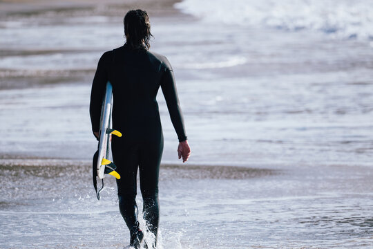Surfer walking into the ocean with surfboard under arm