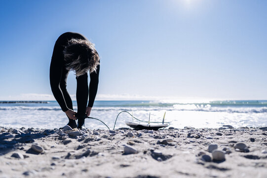 Surfer putting on neoprene socks on the beach on a sunny day