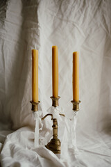 Three beeswax candles in a vintage brass candlestick on a light linen fabric background