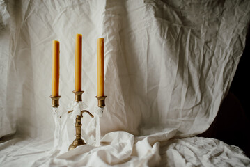 Three beeswax candles in a vintage brass candlestick on a light linen fabric background. Space for text