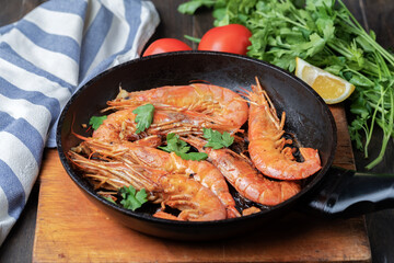 Roasted langoustines in a pan with herbs and garlic. Dark wooden background. View above.