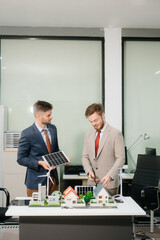 Team of diverse multiethnic businesspeople standing neare table looking at model of building from residential project.