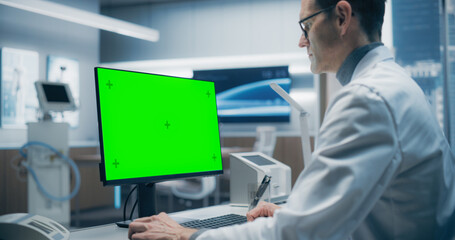 A Male Scientist in a White Lab Coat Analyzes Data on a Green Screen Computer in a Advanced Medical...