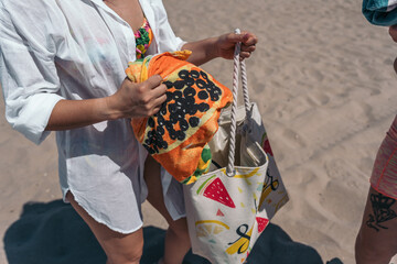 Woman holding colorful beach towel and bag on sand