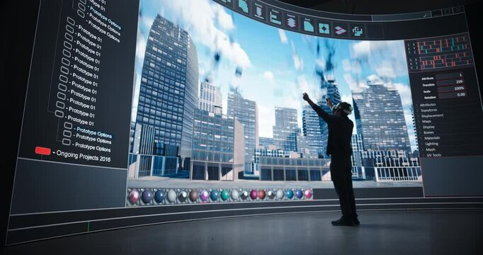 Young Architect Using Virtual Reality Technology, Dynamically Constructs a Digital Cityscape on a Massive Screen in a Dark Studio. Creative Man Wearing a VR Headset and Holding Motion Controllers