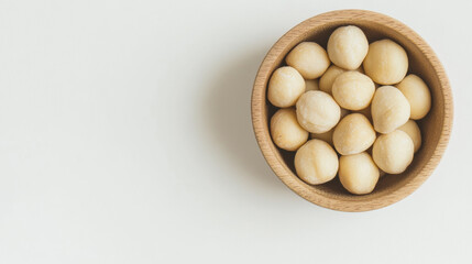 Natural macadamia nuts in wooden bowl on light background, showcasing their creamy texture and round shape, perfect for healthy snacking
