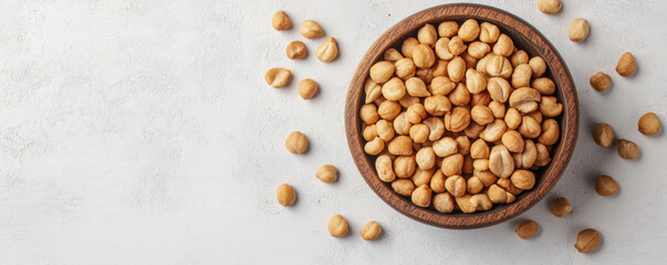 Top view of macadamia nuts in round wooden bowl, surrounded by scattered nuts, showcasing their natural texture and color. Perfect for healthy snacking or culinary use