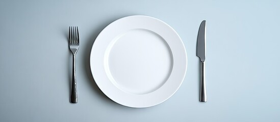 Elegant white plate positioned center with fork left and knife right, minimalist design on light blue table, ideal for fine dining imagery.