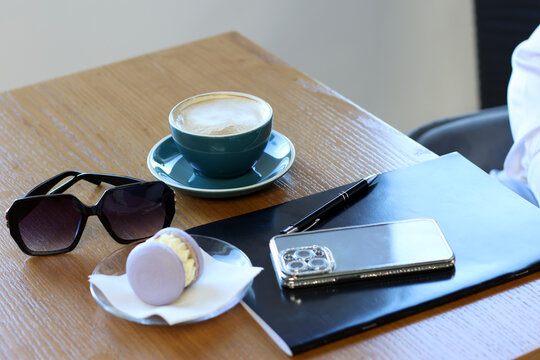 Cafe table with coffee and donut, notebook, smartphone and sunglasses.