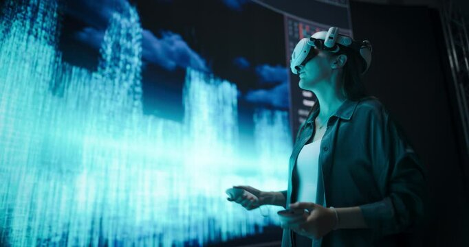 Young Female Architect Creates a Parametric Design of a Big Futuristic City with Skyscrapers. Artist Wearing a Virtual Reality Headset and Interacting with a Digital Polygon Mesh on a LED Screen