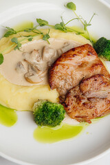 Grilled chicken breast is served with creamy mashed potatoes, steamed broccoli florets, fresh pea shoots, and a rich mushroom sauce. Restaurant or cafe menu, cookbook recipe