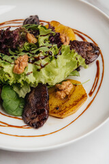 Warm salad featuring roasted veal, caramelized pear, fresh lettuce, and crunchy nuts drizzled with balsamic sauce on a white plate atop a marble table. Restaurant or cafe menu, cookbook recipe