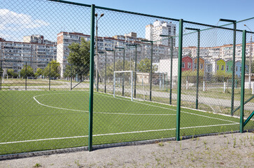 Lawn field for playing football behind the green fence mesh at school territory. Close-up of soccer field with green grass
