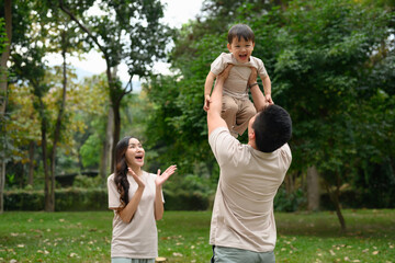 Fototapeta premium Happy father lifting his little son into the air enjoys spending leisure time together at outdoor