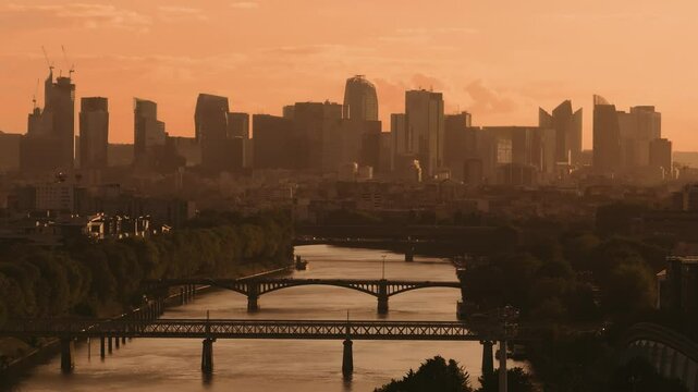 Vue sur les tours de La D&eacute;fense et la Seine &agrave; Saint Ouen au coucher du soleil avec de la circulation de voitures, de m&eacute;tro et de passants sur les ponts. 