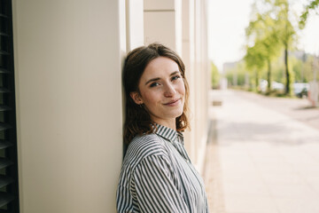 Young woman leaning against wall looking at camera