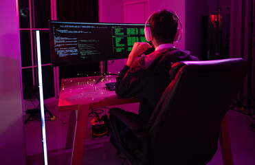 Individual immersed in coding at a computer workstation with vibrant lighting in a modern setting