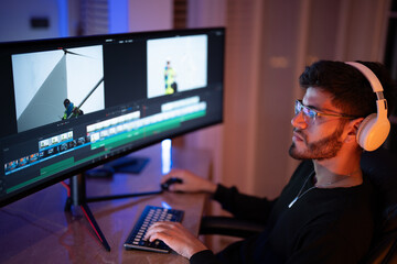 Young man engaged in video editing using dual monitors with professional software in a dimly lit workspace