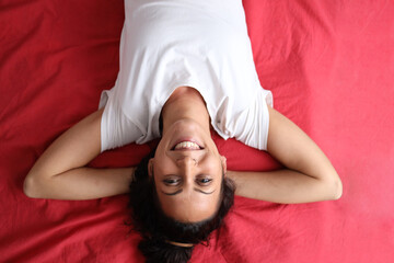 Young woman lying upside down on red bed smiling with hands behind head