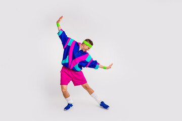 Energetic young man in colorful vintage activewear practicing dynamic moves against a white backdrop, exuding happiness and style