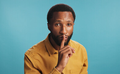 Black man, finger and shush noise in studio, confidential mystery and private announcement. Male...