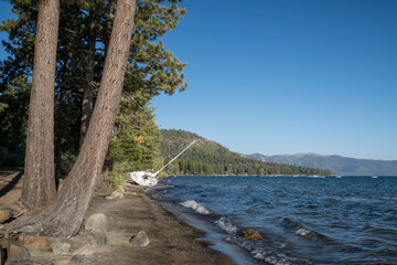 A beach on the shore of Lake Tahoe, California. A sail boat seems to be washed up on the shore