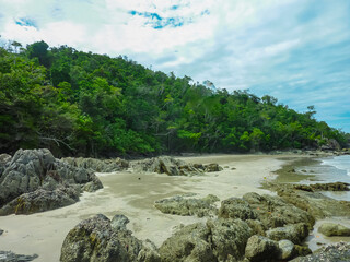 Obraz premium Tranquil rocky beach with turquoise waters along tropical coastline in Cairns, Australia. Lush green rainforest meets sandy shore dotted with volcanic rocks. Dramatic natural landscape, Pacific Ocean
