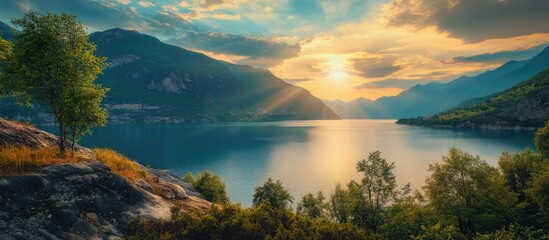 Fototapeta premium Serene lakeside landscape at sunset with mountains in the background, vibrant orange and blue hues reflecting on calm waters surrounded by lush greenery