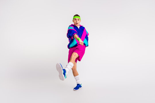 Energetic young man in vibrant retro sportswear doing dynamic exercise with a joyful expression on a white background - Powered by Adobe