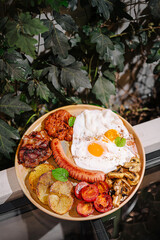 Delicious breakfast platter featuring eggs, bacon, sausage, and vegetables served outdoors among lush greenery