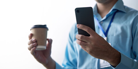 Business professional holding a smartphone and coffee cup, showcasing multitasking and modern communication in a contemporary office setting.