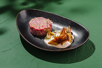 Delicious tartare with unique garnishes served on an elegant plate against a vibrant green background
