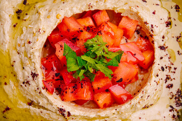 Fresh hummus topped with diced tomatoes and herbs served in a bowl with a drizzle of olive oil