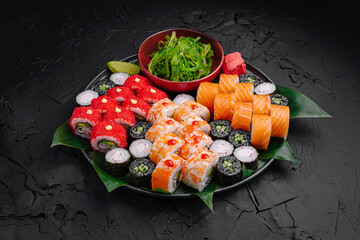 Delicious sushi platter featuring various rolls and sides on a dark textured surface © AntAlexStudio