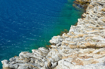 Rugged limestone shoreline meets vibrant blue sea, creating stunning contrast of textures and colors. Clear water reveals underwater rock formations, highlighting natural beauty of coastal landscape