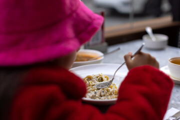 Chilly Evening, Cozy Dish: Girl Enjoys Pasta in a Fur Coat at Outdoor Cafe