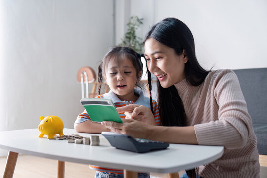 Diverse mother and daughter learning about saving money together with a yellow piggy bank, calculator, and notebook at home, enhancing financial skills.