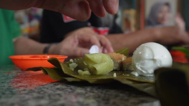 A closeup of men's hand eating together at a tofu restaurant in Sumedang, West Java, Indonesia. Fried tofu is eaten with lontong and salted egg, served with sambal or dipping sauce