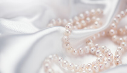 Pearl necklace over white silk background, close up. Beautiful Natural pearls beads, elegant accessories. Wedding concept, Valentine's Day Gift. 
