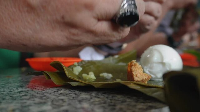 A closeup of men's hand eating together at a tofu restaurant in Sumedang, West Java, Indonesia. Fried tofu is eaten with lontong and salted egg, served with sambal or dipping sauce