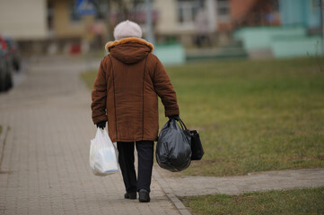 an elderly woman walks down the street with heavy bags