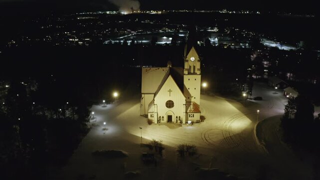 Zoom Out Drone Footage of Illuminated Church In a Snow-Covered Town at Night, Surrounded by Glowing Lights, Serene Winter Scenery, Religion and Christianity in Pite&aring;, Sweden