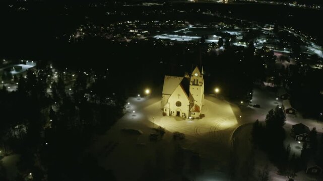 Drone Footage of Illuminated Church In a Snow-Covered Town at Night, Surrounded by Glowing Lights and Serene Winter Scenery, Religion and Christianity with Peaceful Atmosphere in Pite&aring;, Sweden