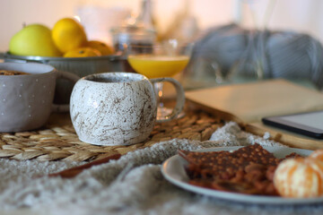 Books, e-reader, tea, orange juice, fruit, snacks, yarn, blanket and lit candles on the table. Autumn or winter hygge at home. Selective focus.