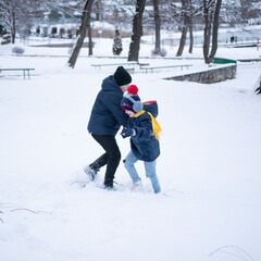 Two children, bundled in warm winter clothes, playfully interact in a snow-covered park. The older...