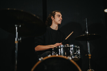 A young man intensely playing drums in a dark music practice room, showcasing talent and dedication...