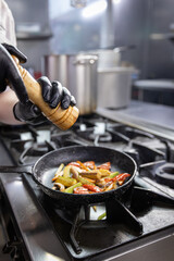 Chef grinding spices into a pan of grilled vegetables